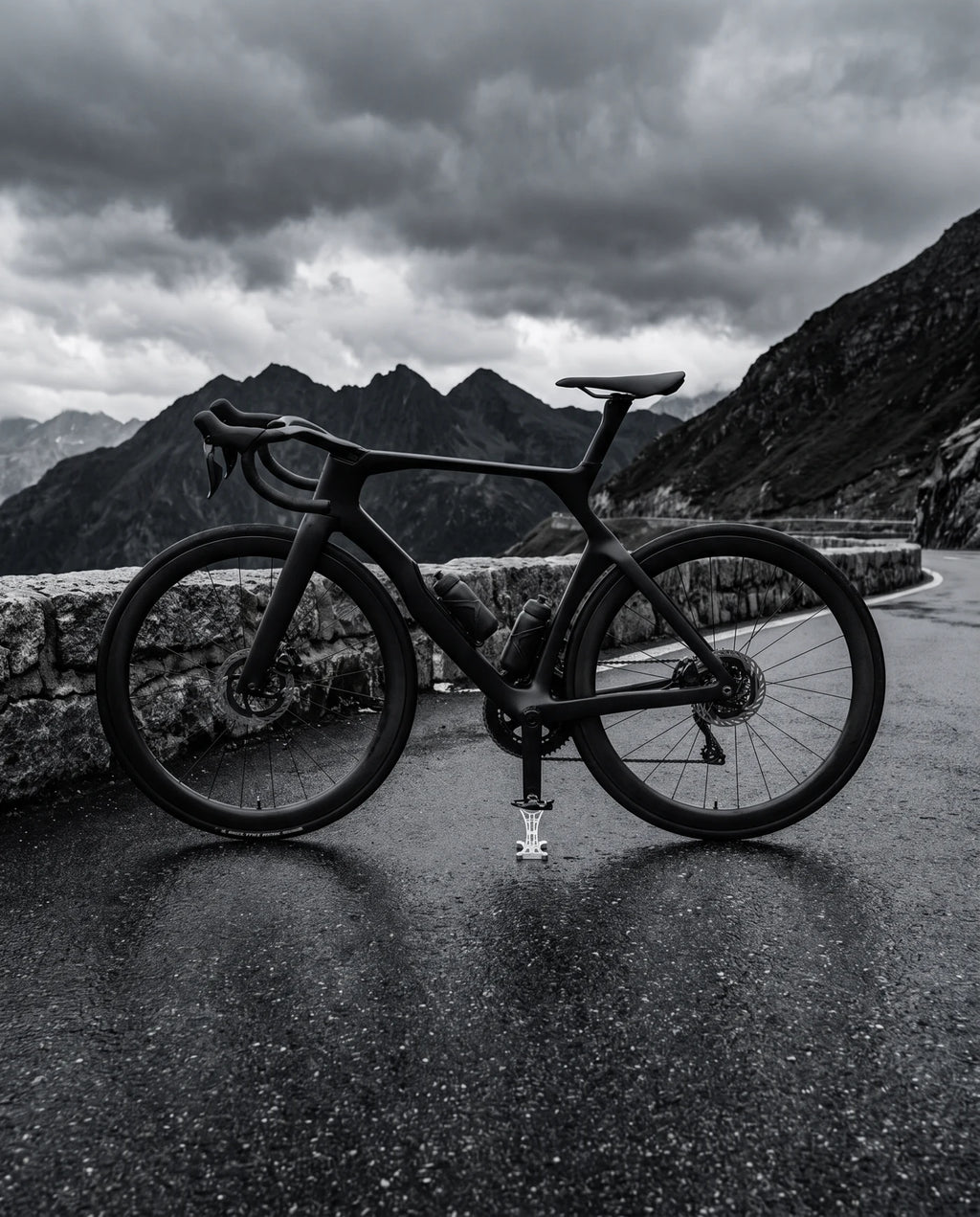 Black road bike on THE STAND 0.01 on a mountain pass road under a storm sky